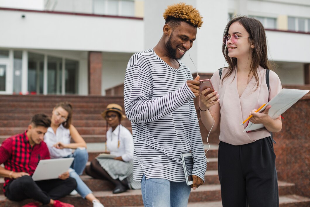 Estudantes interagindo com celular e materiais de estudo nas escadas de uma universidade
